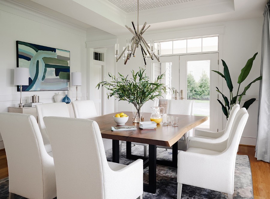 A dining room with white chairs and a table. A square table promotes more interaction because each guest can see everyone’s face.